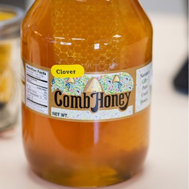 Shilo+-+HoneyStore-12 Clover Comb Honey in a clear jar showcasing honeycomb structure, with a colorful label indicating natural sweetness and nutritional information.