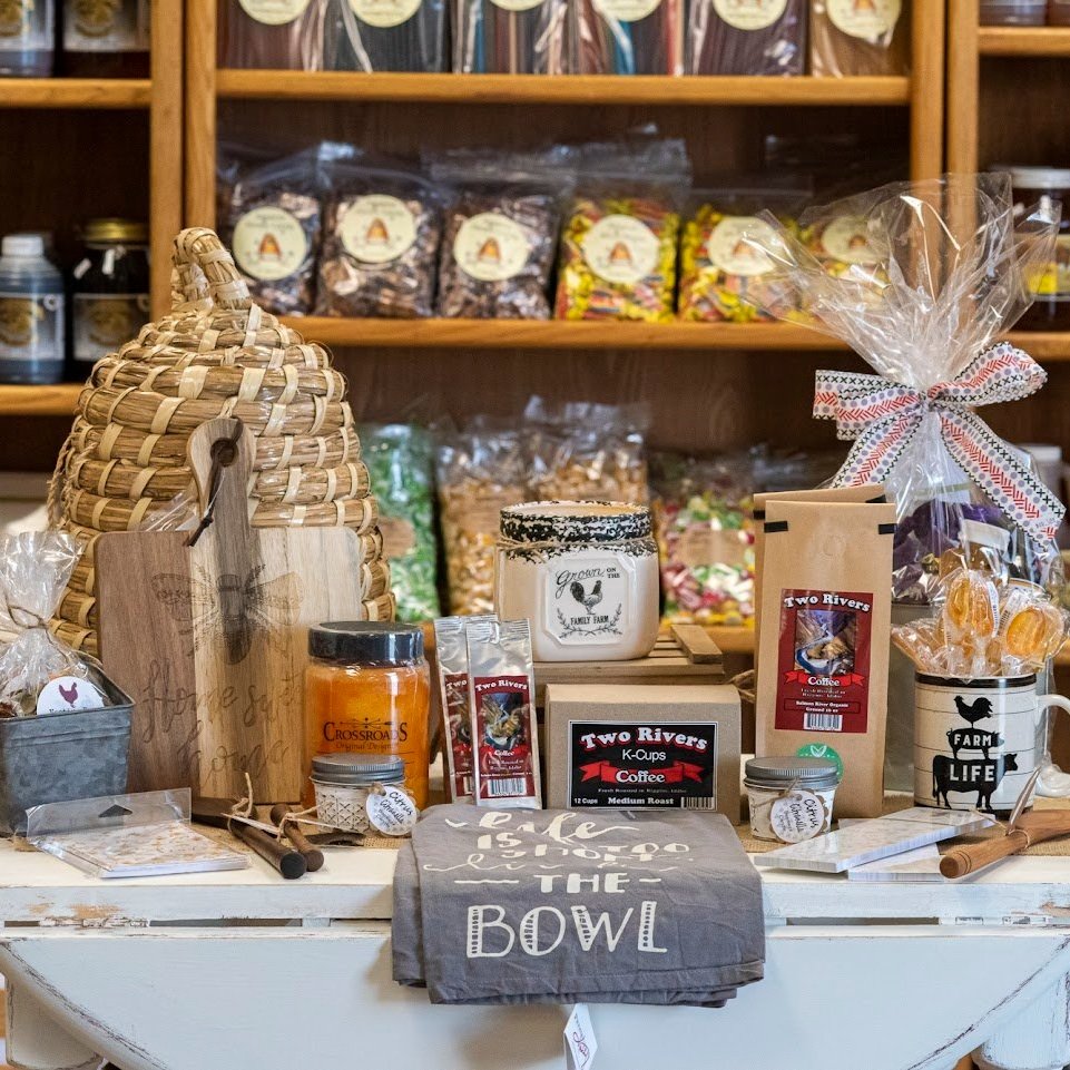 A cozy display of artisanal products including a woven beehive, gourmet coffee, candles, and decorative kitchen items, set against a backdrop of colorful snacks in jars, ideal for a rustic gift shop atmosphere.
