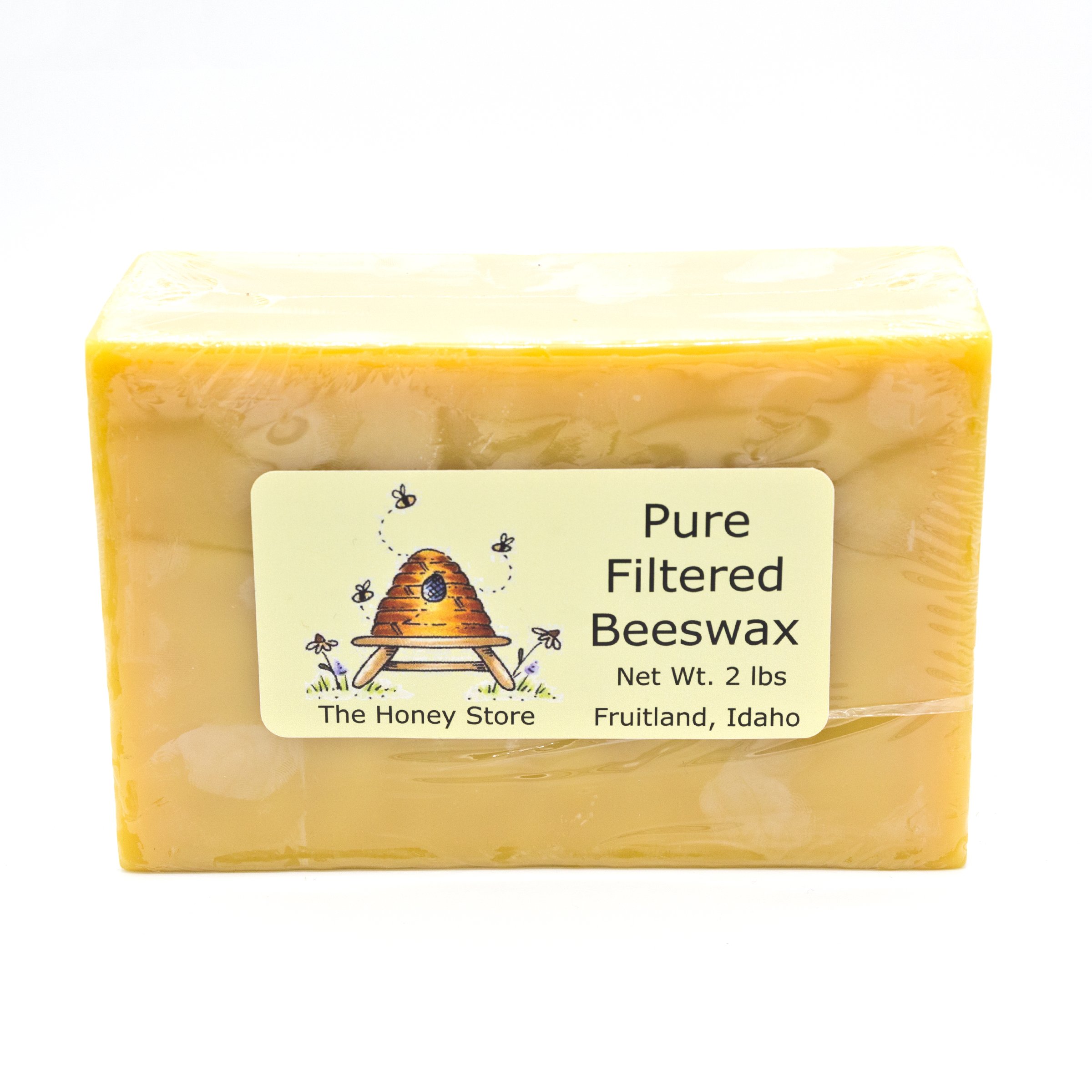 Pure filtered beeswax bar from The Honey Store, weighing 2 lbs, packaged in clear wrap, featuring a label with a honeycomb illustration and details from Fruitland, Idaho. Ideal for crafting, candles, and natural skincare.